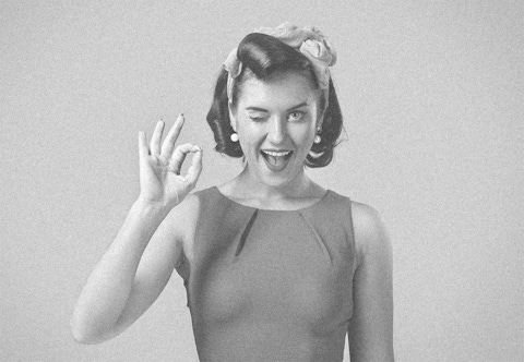 Photo of a woman from 1960s holding a birth control pill and winking.