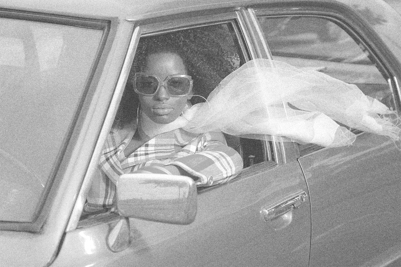 Vintage photo of an African American woman in a 1970's car driving.