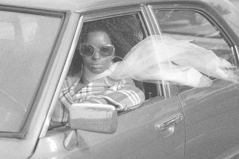 Vintage photo of an African American woman in a 1970's car driving.