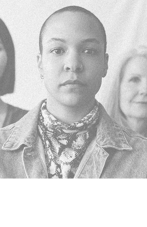 Black woman looking starkly into the camera with women on either side of her in the background.