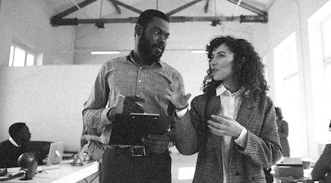 A man and woman talking in a classroom with the man writing notes on a clipboard.