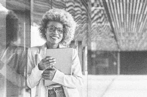 African american business woman leaning up against a corporate building holding her laptop and smiling