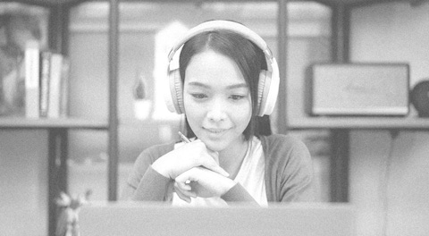 Woman looking at her computer wearing headphones.