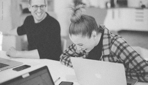 Colleagues in a meeting with computers open, laughing.