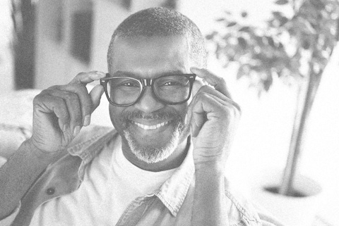 Man putting on glasses and looking at the camera, smiling.