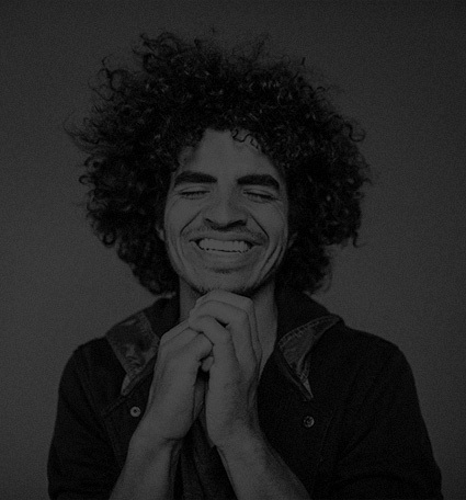 Man with curly hair smiling with his eyes closed.