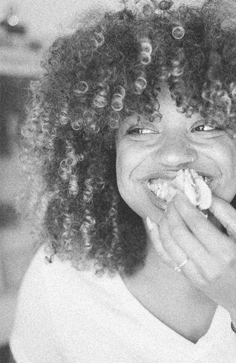 Woman with curly hair smiling and eating.
