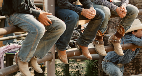 Three cowboys sitting on a fence in jeans and boots