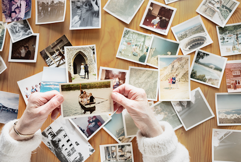 An elderly woman is fondly looking back at memories past in a collection of photos on the table.
