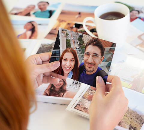 Woman looks intently at a vacation photo of her and her partner while scrapbooking a photo album.