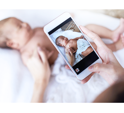 Parent taking pictures of a newborn on their smart phone.