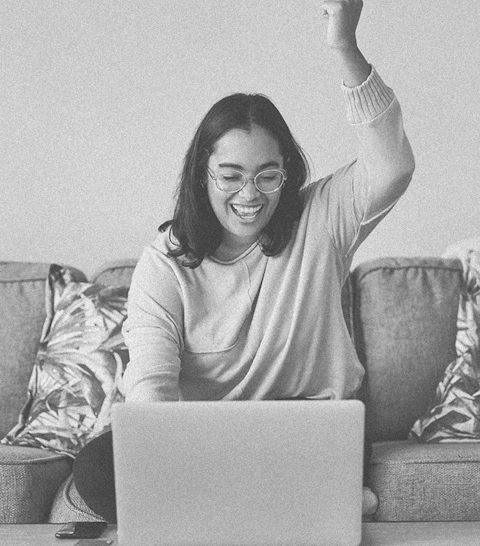 Woman working at her computer, smiling and raising her left arm, cheering.