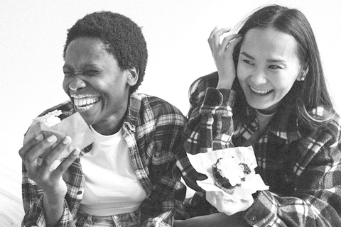 Two women eating cupcakes together and laughing.